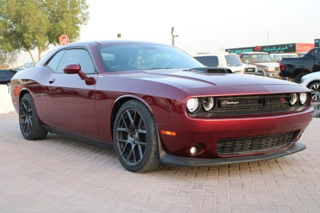 Dark red Dodge Challenger muscle car parked on brick paving with LED headlights and body kit