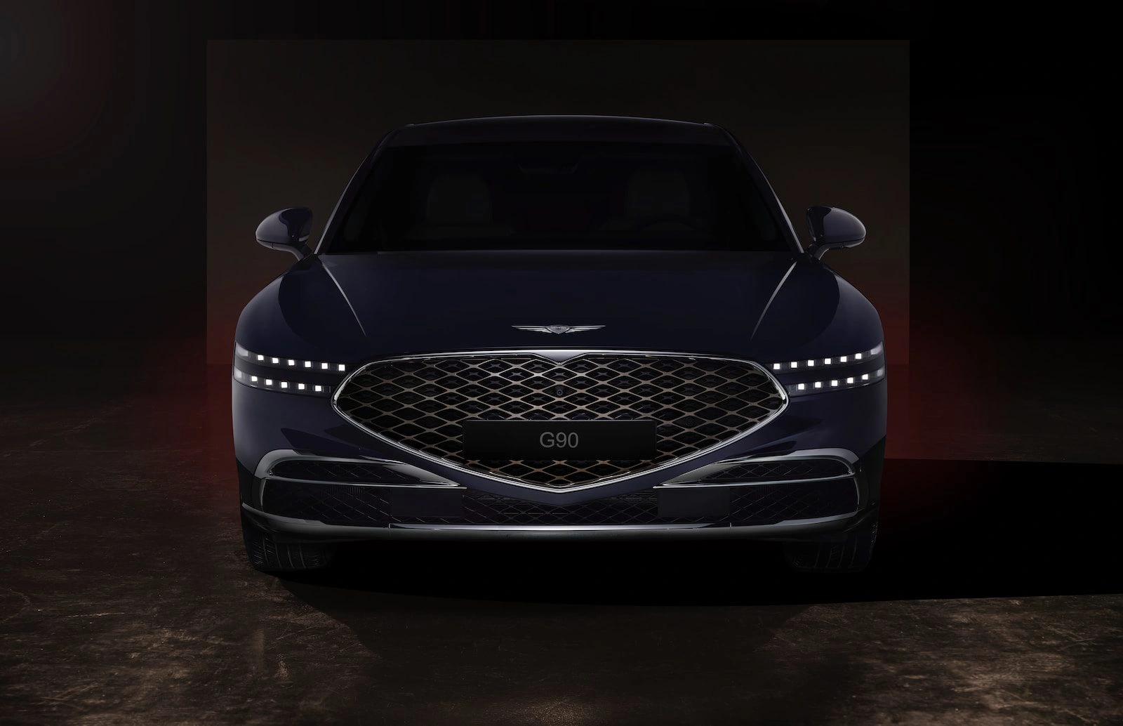 Genesis luxury sedan front view with diamond-pattern grille and LED headlights in dramatic dark studio lighting