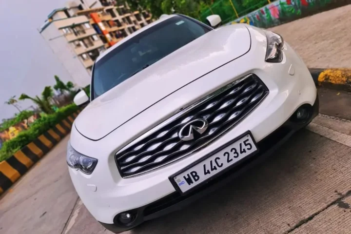 White Infiniti QX80 luxury SUV parked on street with industrial warehouse background and yellow safety stripes